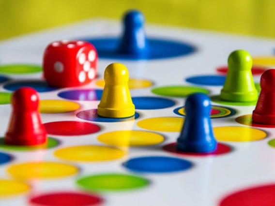 Colorful board game with blue, red, and yellow game pieces and a rolling die
