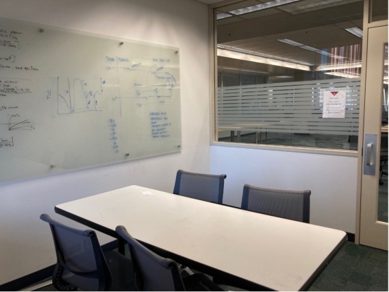 Table and four chairs in a study room with a whiteboard and a glass wall