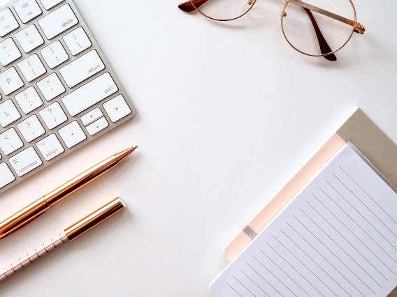 partial view of a keyboard and a pad of paper, with pen, pencil and eyeglasses