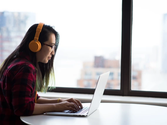 Woman wearing headphones, typing on a laptop