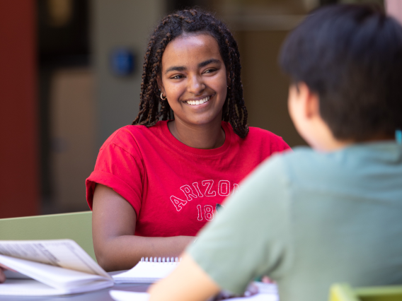 Student smiling at another student, both seated