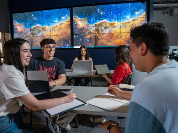 Four students actively discussing and working together around a table in the Data Studio