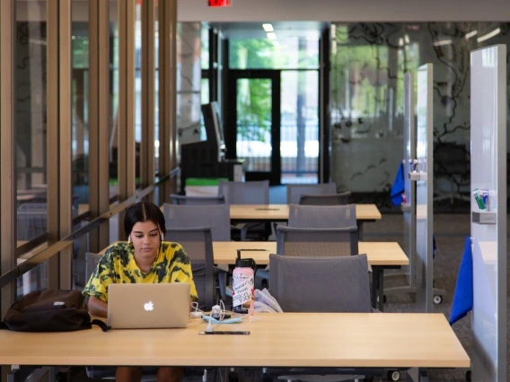 student in yellow shirt working on laptop in library