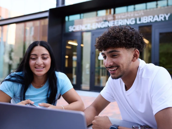 Two students looking at a laptop outside in the sunlight by UA Science Engineering Library