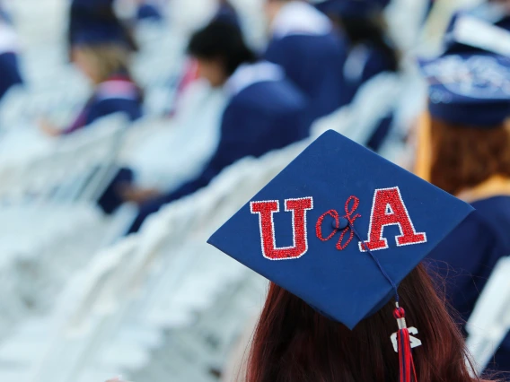 A graduation crowd with the main subject's back to the camera and "U of A" on their cap