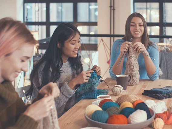 Three people sitting at a table and knitting together