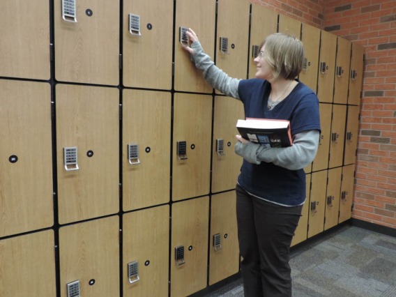 Woman holding books trying to unlock a lock in front of three rows of lockers