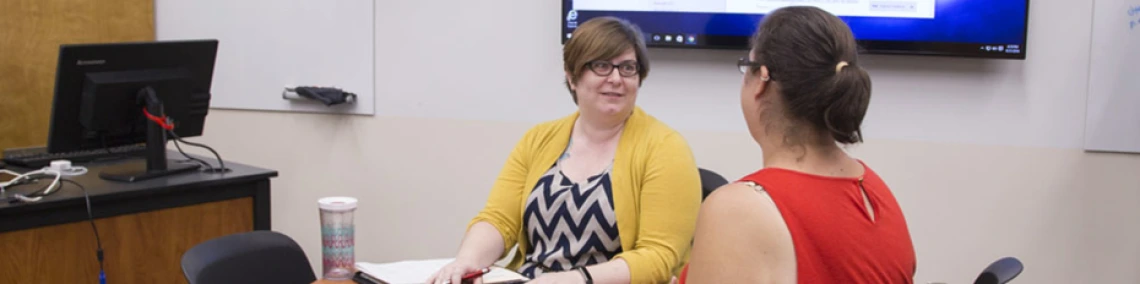 Two faculty members are talking in a classroom with computers.