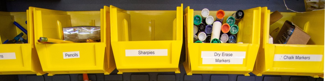 Several boxes in a cabinet that includes pencils, sharpies, and dry erase markers.