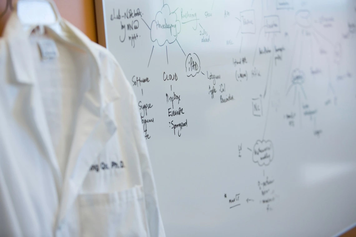 A person wearing white coat standing in front of a whiteboard