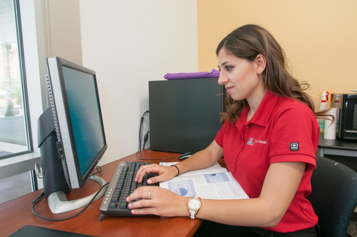 person in red shirt working at desk computer