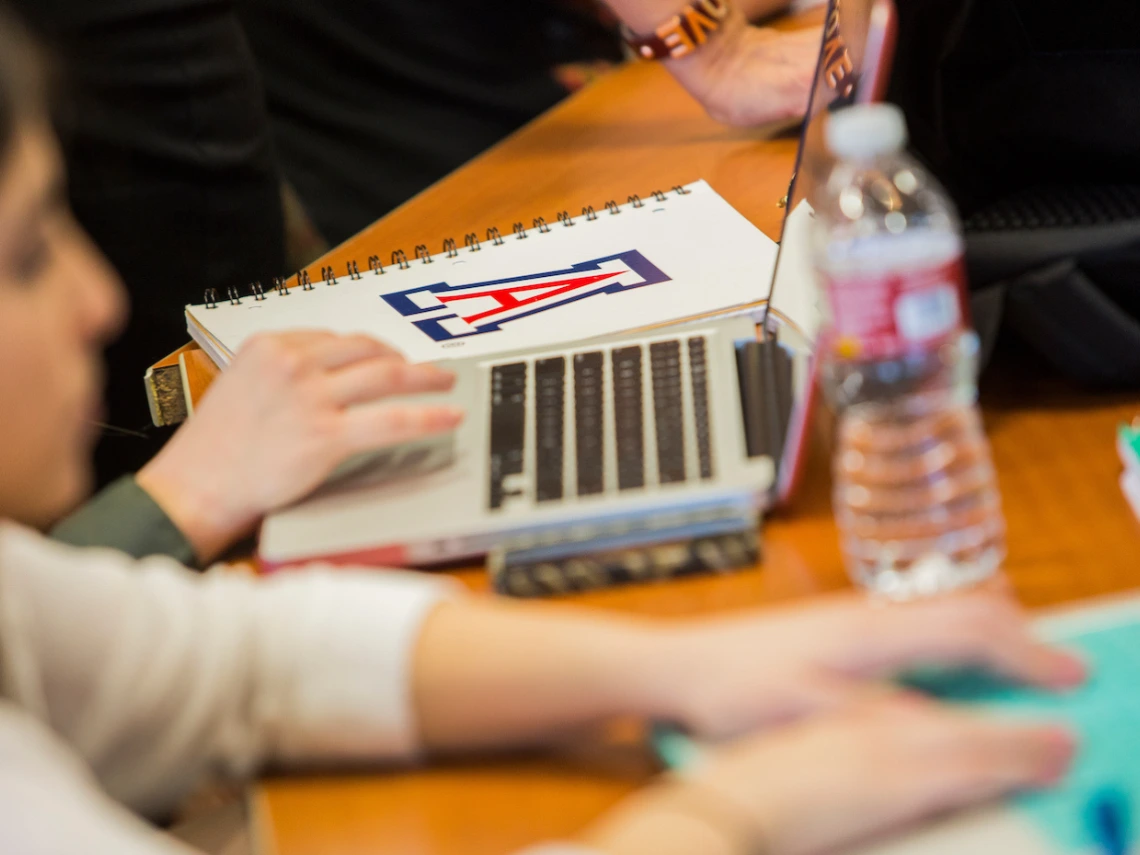 hands working on laptops on a table next to a notebook