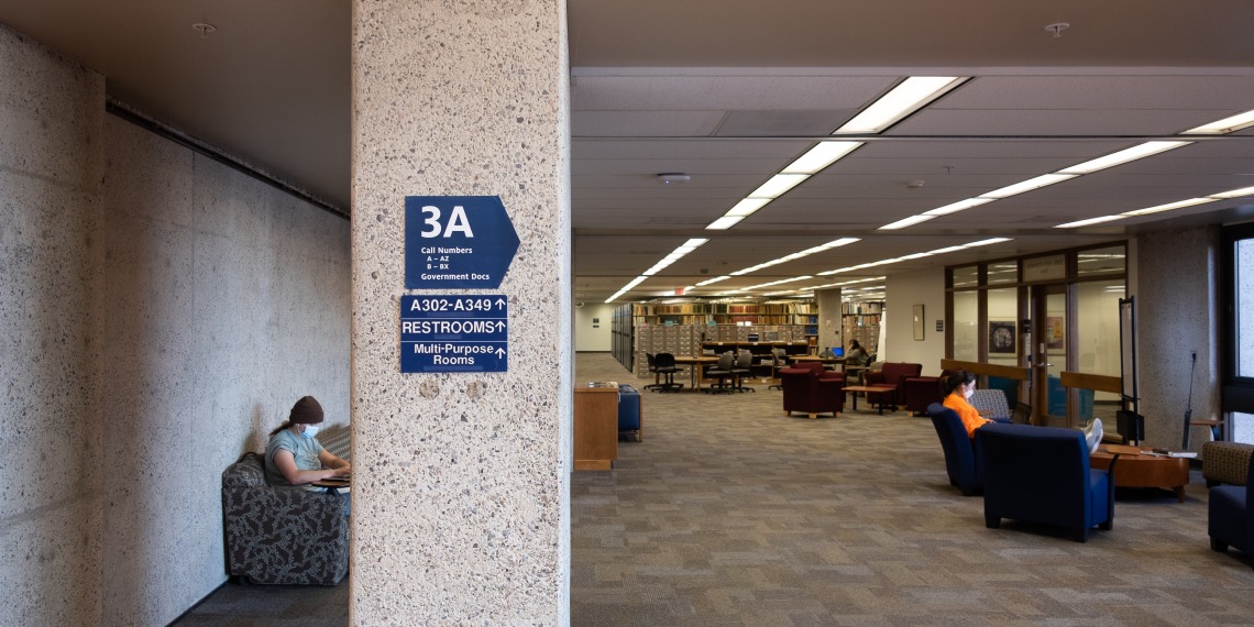 Wayfinding signage on Main Library 3rd floor with people reading in the background