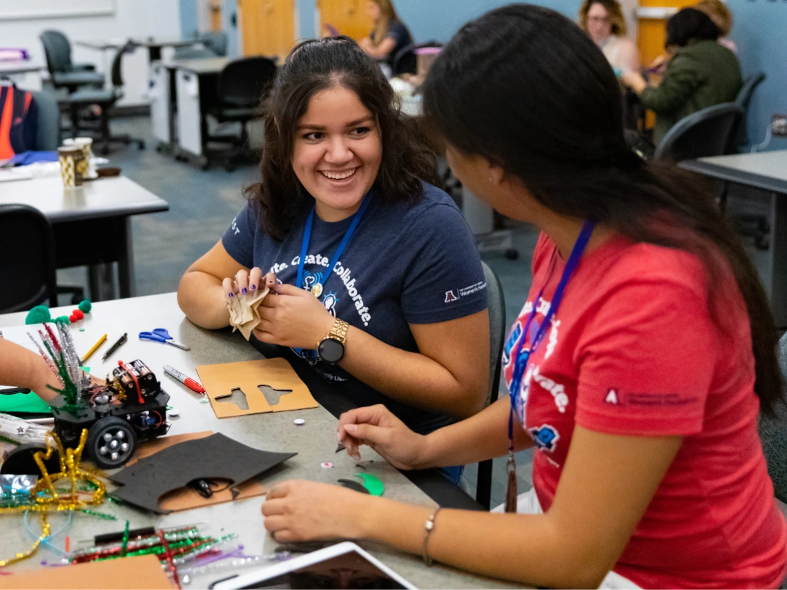 Two female students sitting at a table working on creative projects