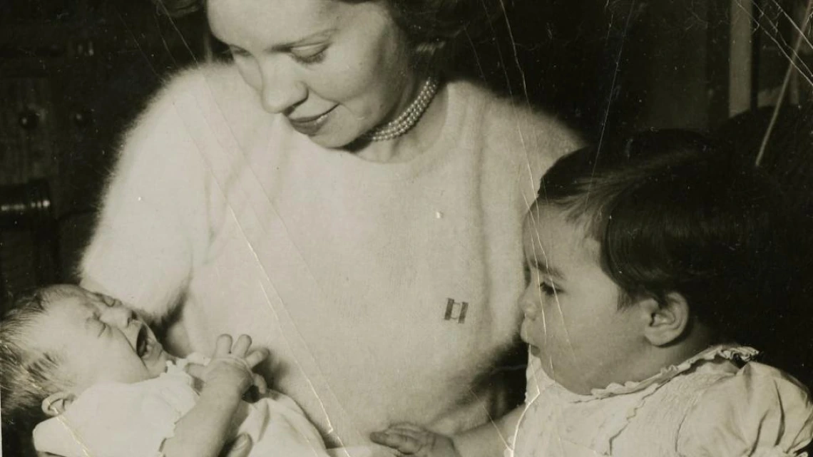 Black and white candid portrait of a woman holding a yawning newborn, a small toddler is at her side looking at the newborn.