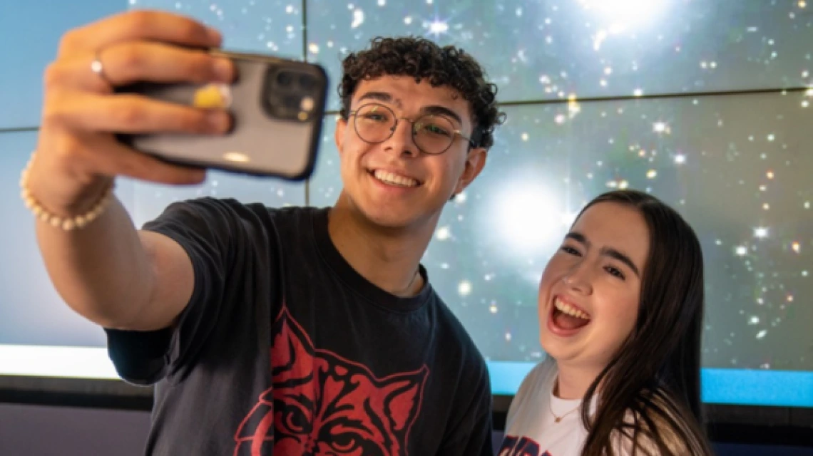 two smiling students taking a selfie in front of Data Studio visualization screen