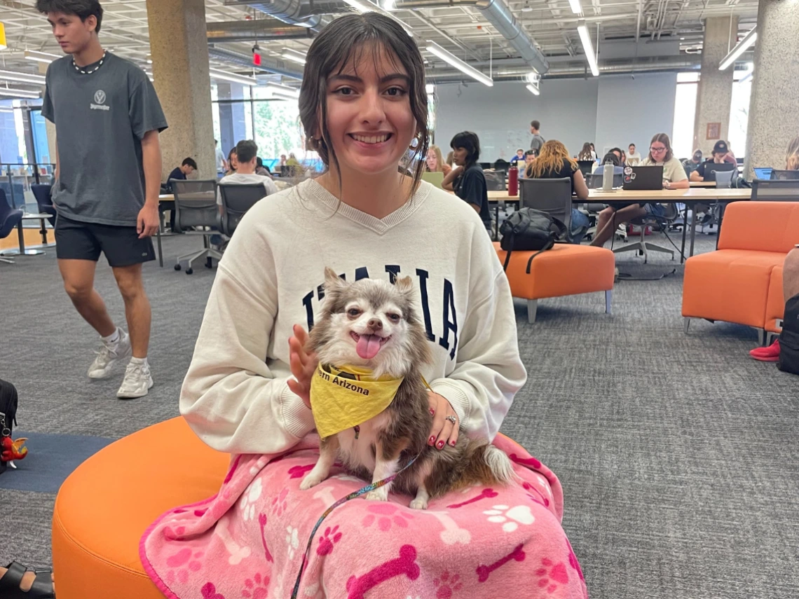 A student poses with a small therapy dog during Pause for Paws