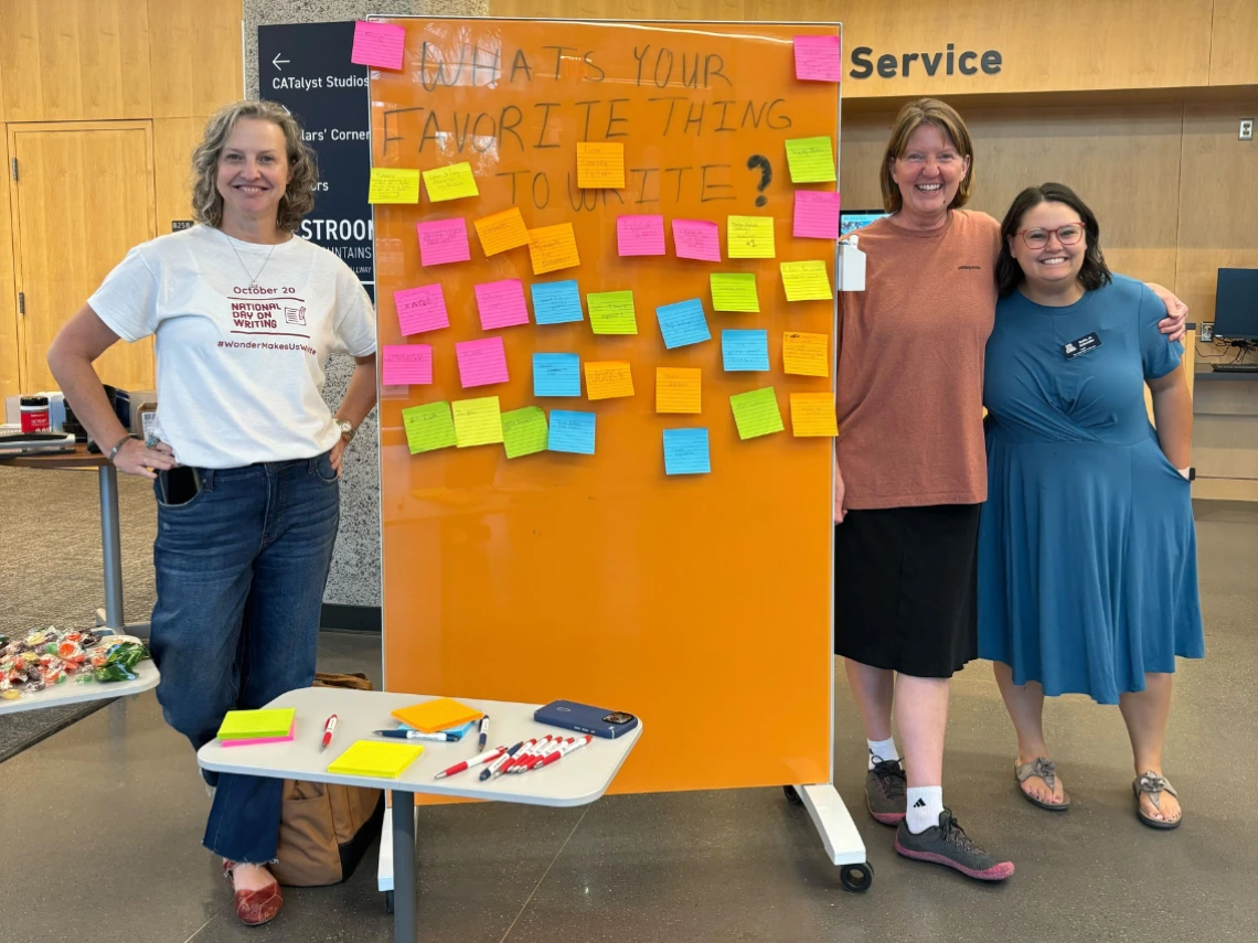 Aimee Mapes, Leslie Sult, Emily Jo Schwaller posing in front of a "talk back board" at National Day on Writing