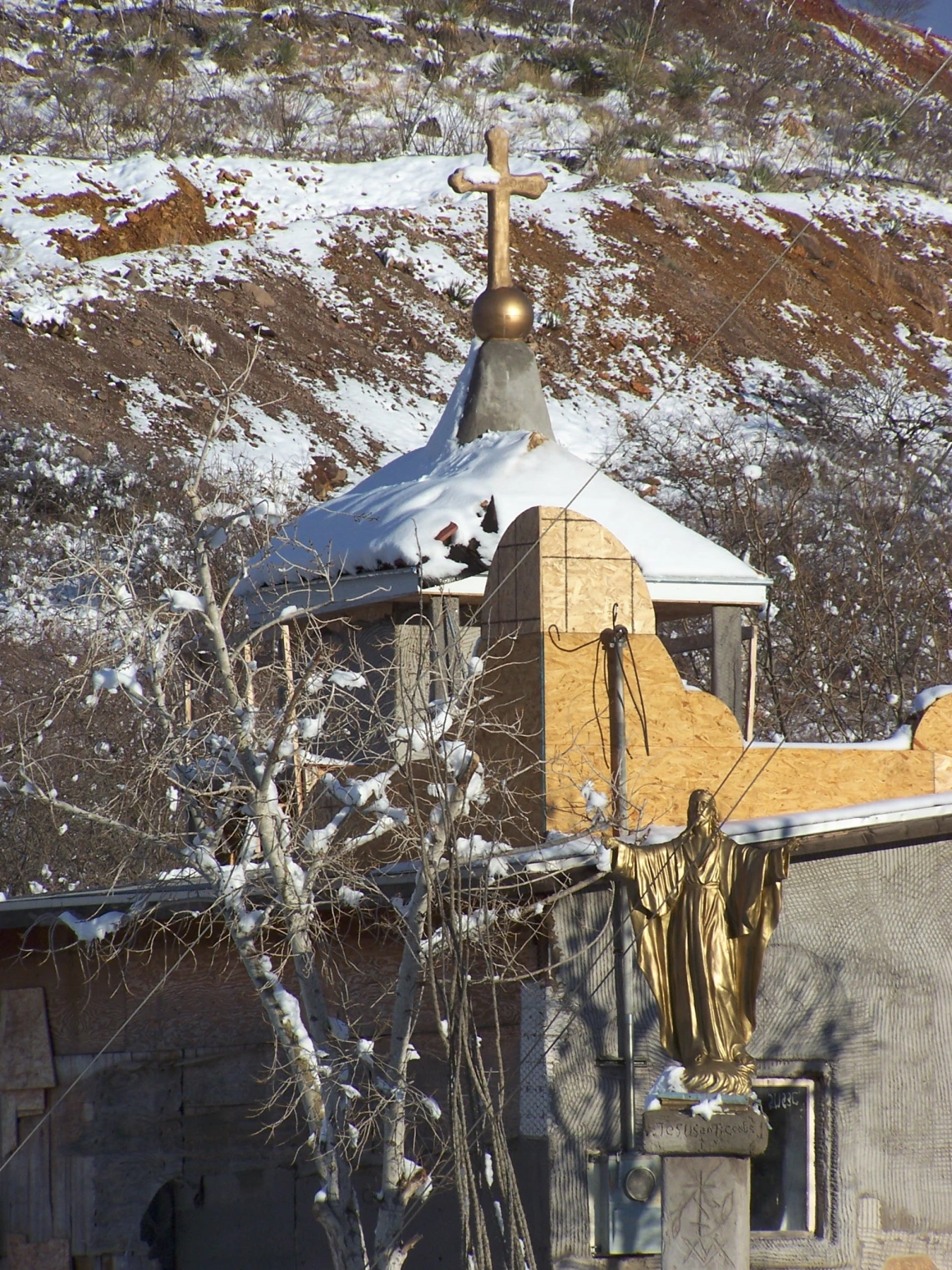 Image of a church steeple and hillside dusted with snow. A gold statue of Jesus stands in the foreground.