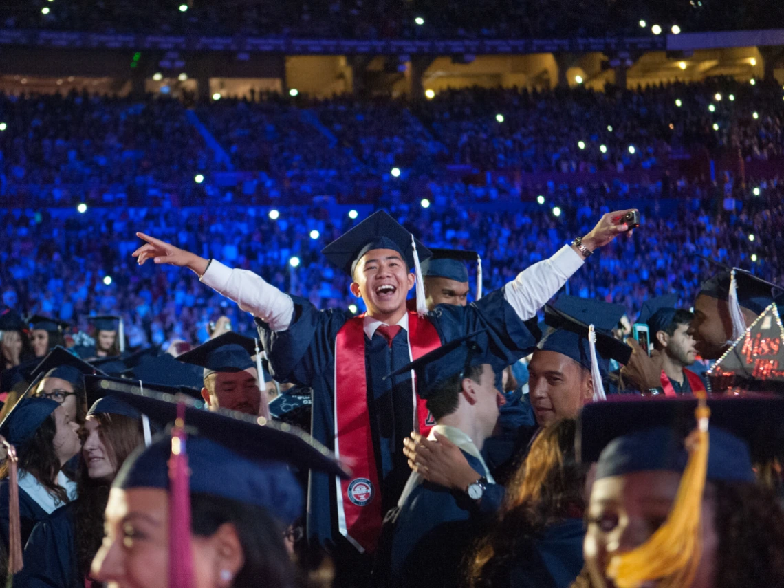 A University of Arizona student at graduation raising his hands up
