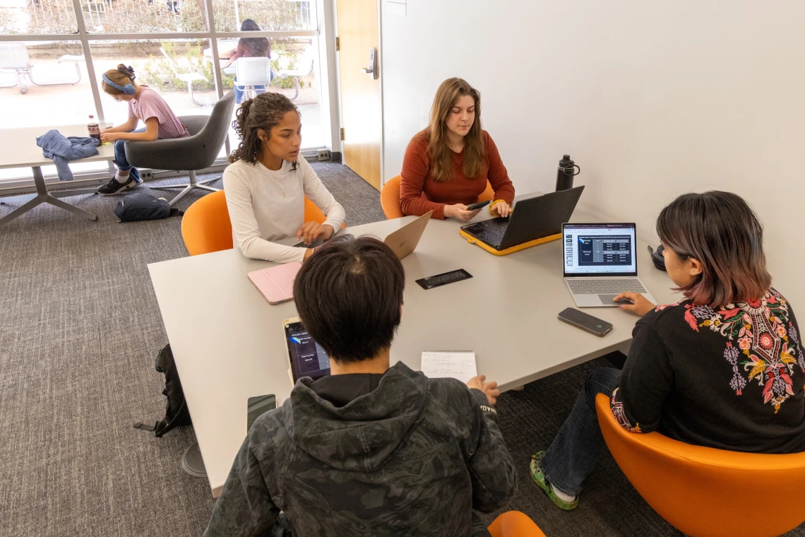 students sitting at a table working on laptops