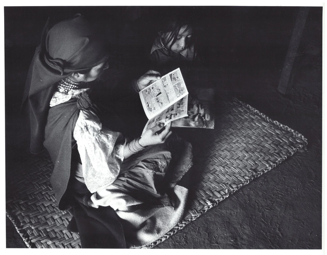 Moody black and white photo of an adult and child sitting on a rug and reading comic books.