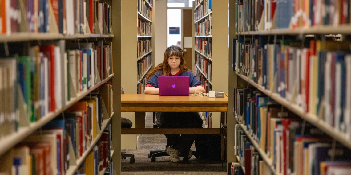 Student sitting and studying with a laptop between stacks