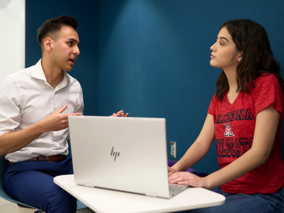 Two people are having a discussion over a laptop