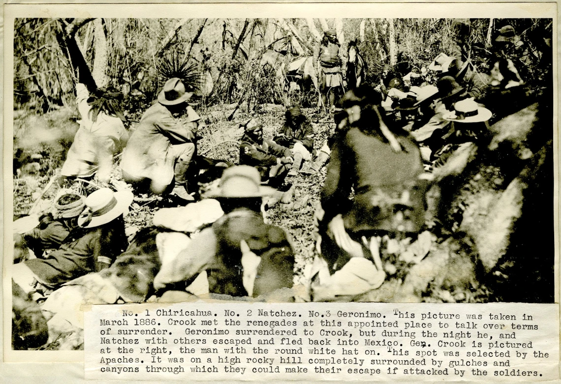 Sepia-toned photo of men gathered in a forest clearing during the surrender of Apache leader Geronimo to General Crook, March 1886.