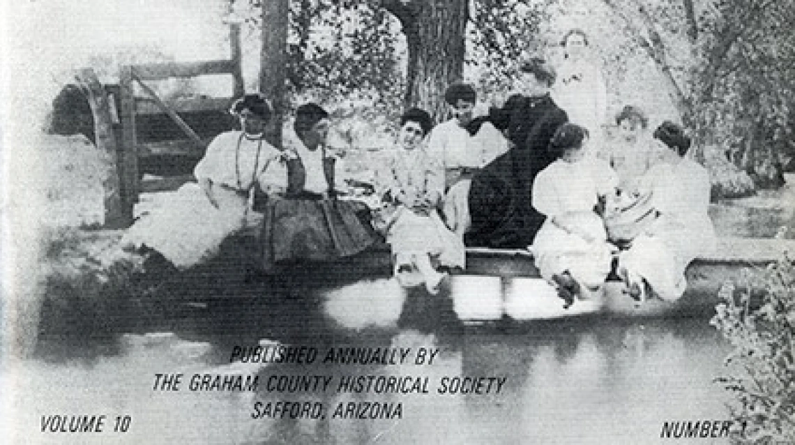 Black and white image of a group of women circa 1890 seated at the edge of a body of water, framed by trees.