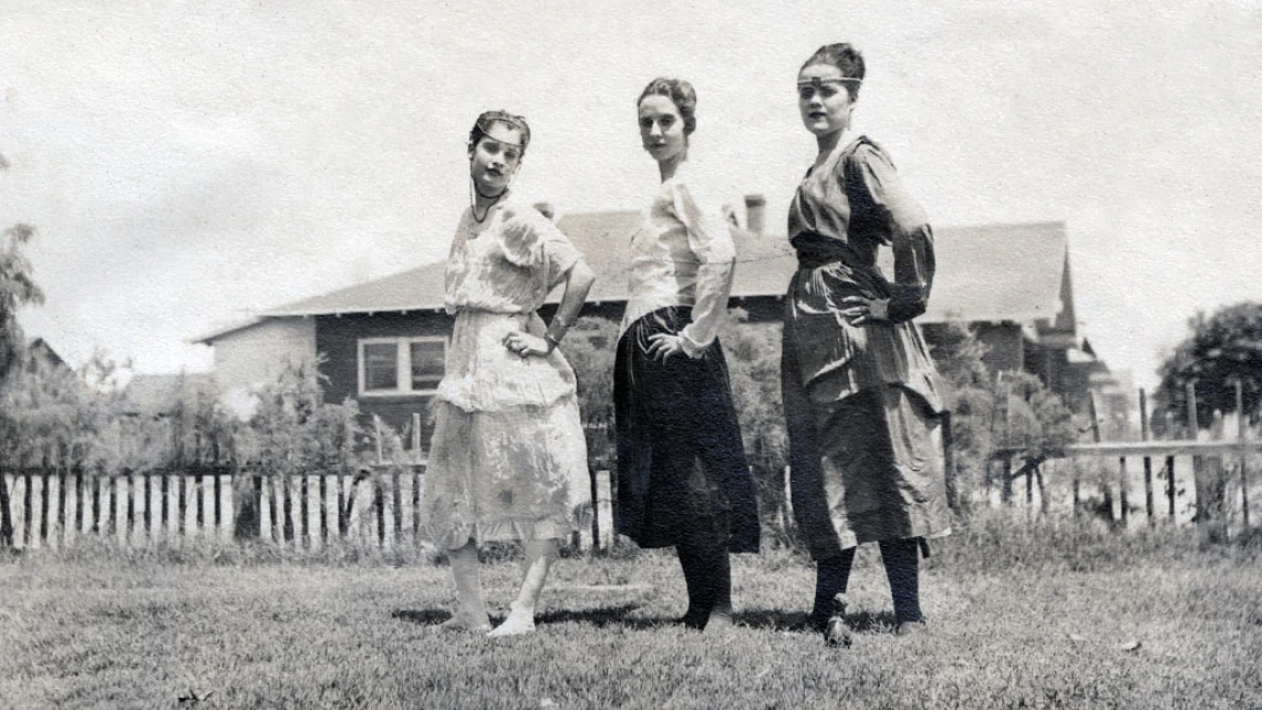 Black and white image of three costumed young women posing in a field, ca. 1918-1925