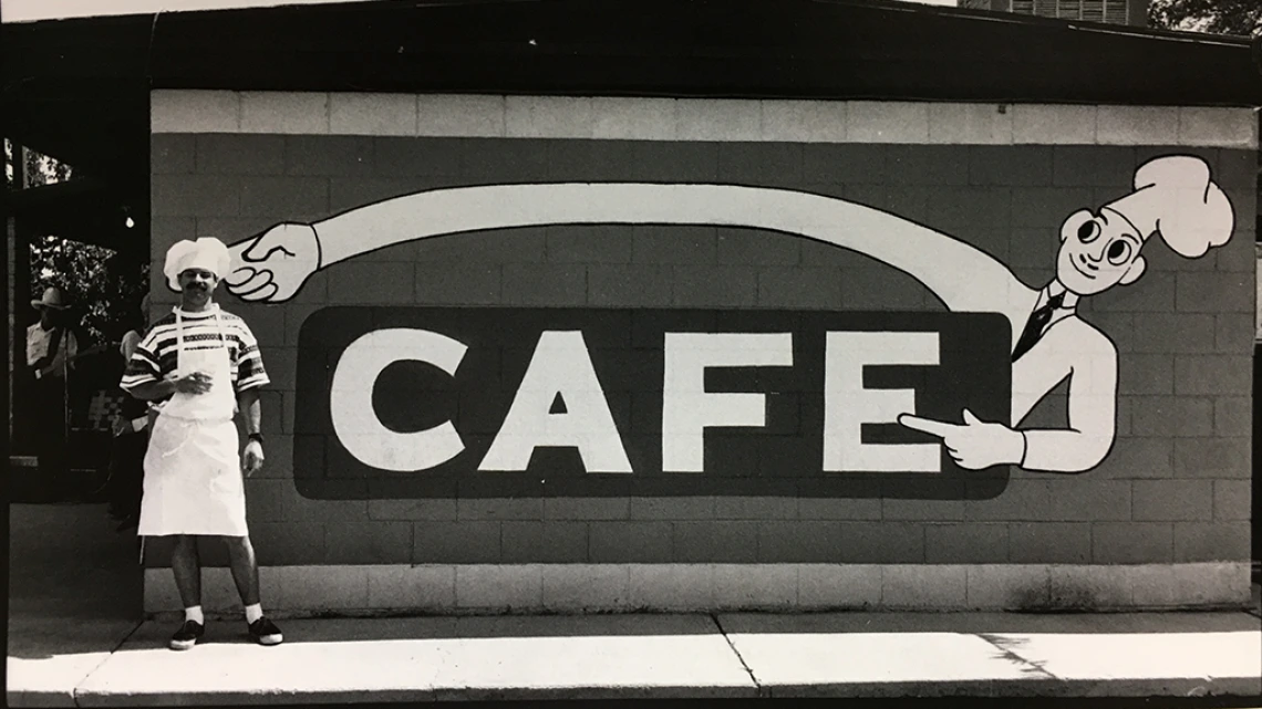 Man in chef hat in front of cafe sign on side of building in Oatman, Arizona