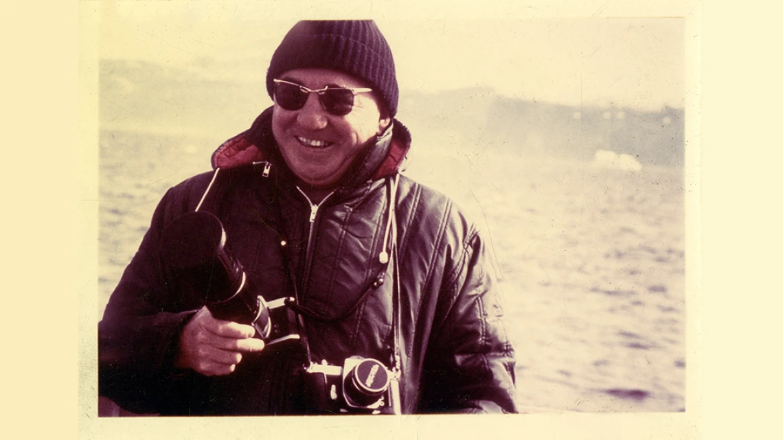 Ray Vicker, circa 1969 Ray Vicker smiling in front of a body of water in Greenland holding two cameras.
