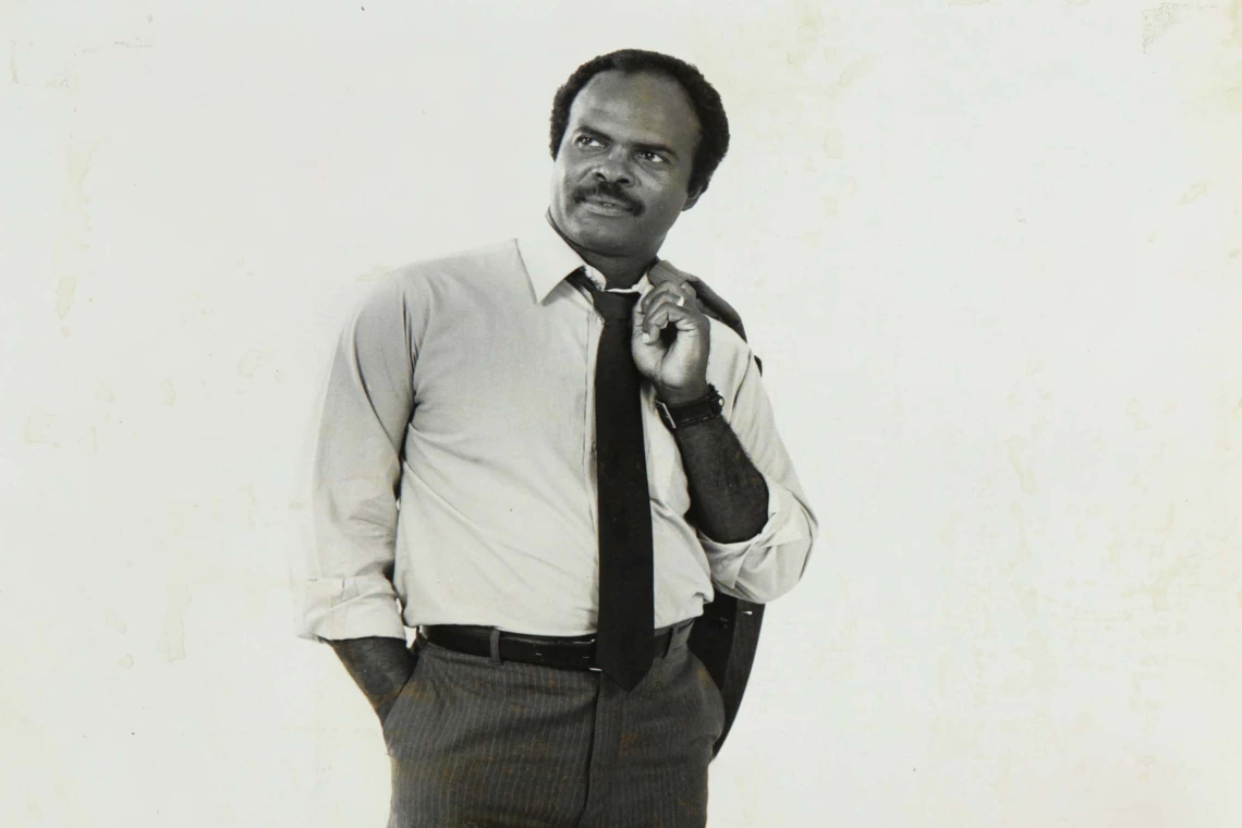 Black and white portrait of Dr. Charles "Chuck" Ford, the first Black Tucson city council member. He looks to his left with his suit jacket slung over his shoulder.