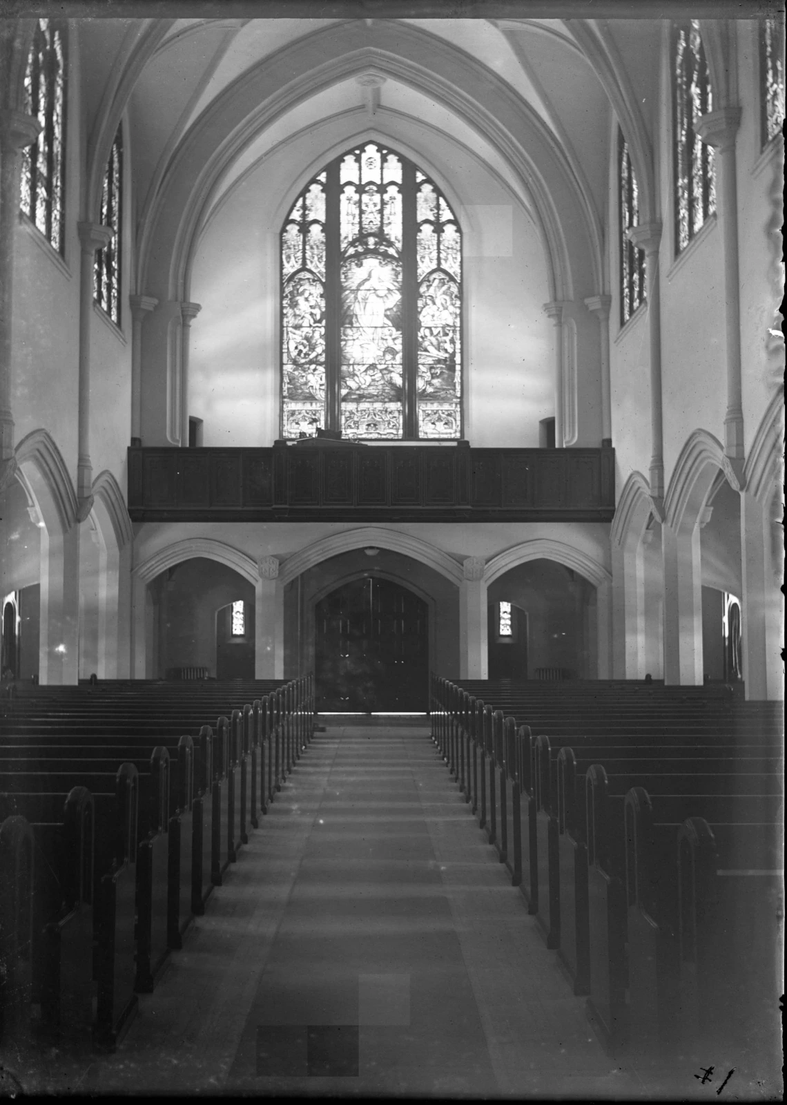 Black and white photo of the narthex of the Bisbee Catholic Church, taken around 1917. The front doors, stained glass window, nave and pews are visible.