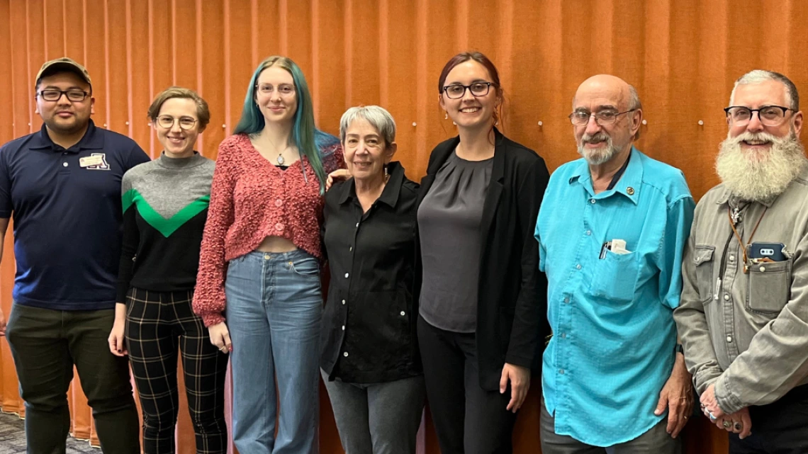 seven people standing against orange backdrop