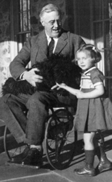 Smiling FDR seated in a wheelchair with a dog in his lap and a young girl at his side