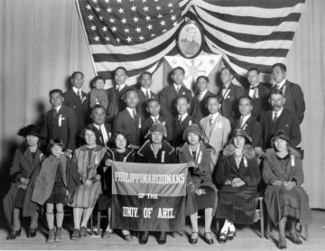 students posing in front of an American and Filipino flag holding a banner