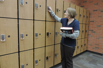 Woman holding books trying to unlock a lock in front of three rows of lockers