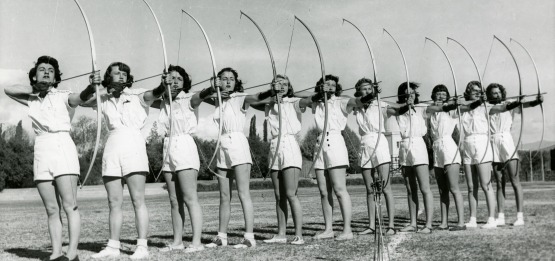 Black and white image of women archers lined up with their bows drawn.